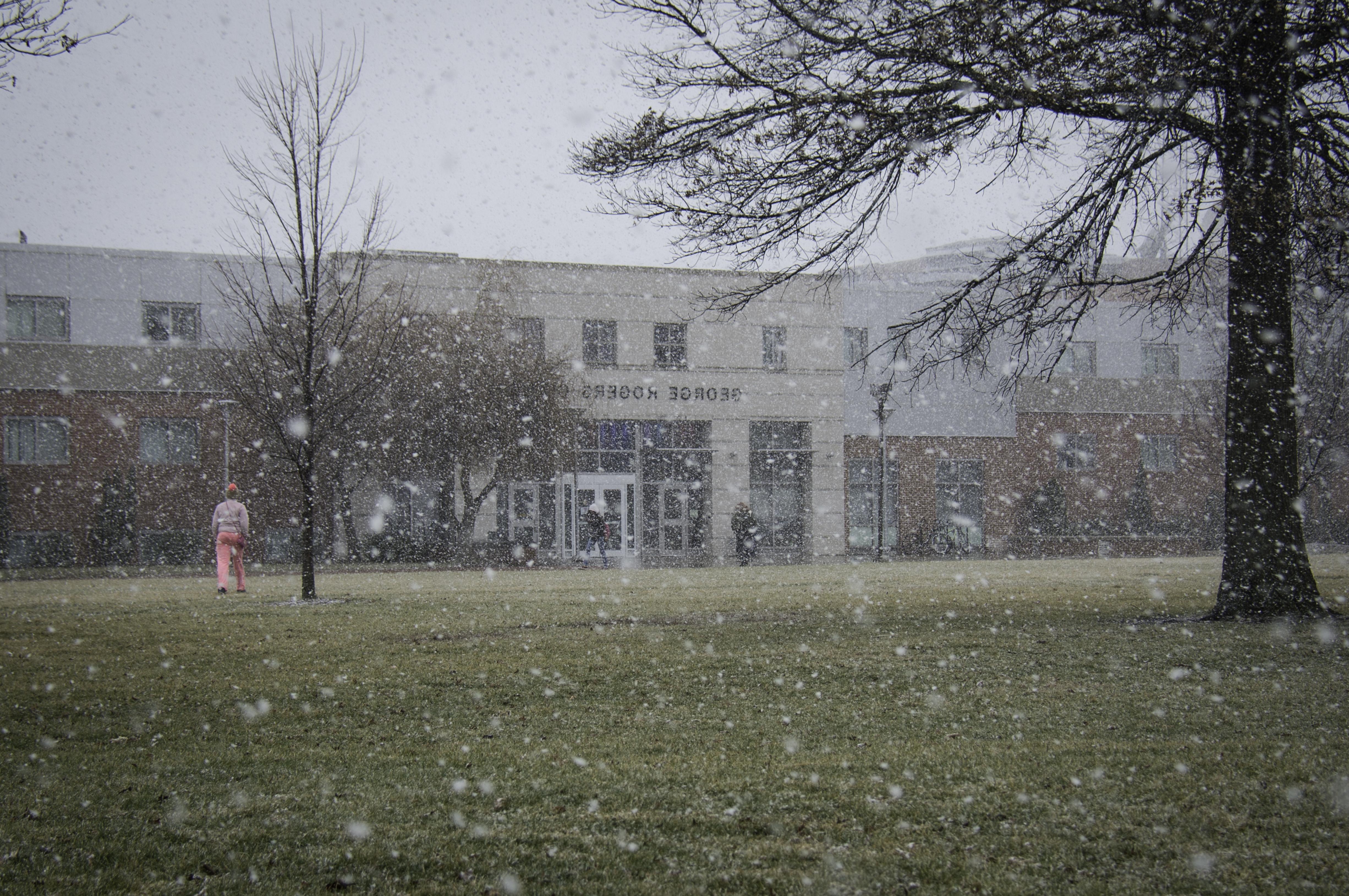 Snow falls in the forefront with Clark Hall and multiple people in the background.